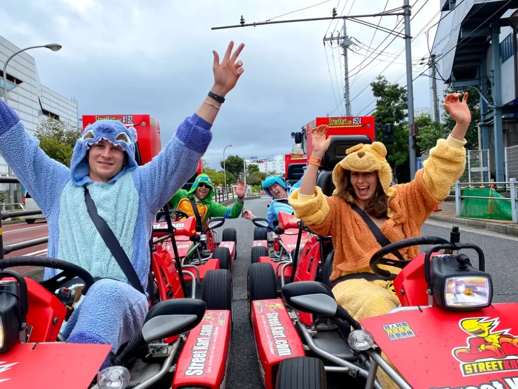 IMG_6133 - StreetKart People in colorful animal onesies riding red go-karts down a city street, waving arms and smiling.