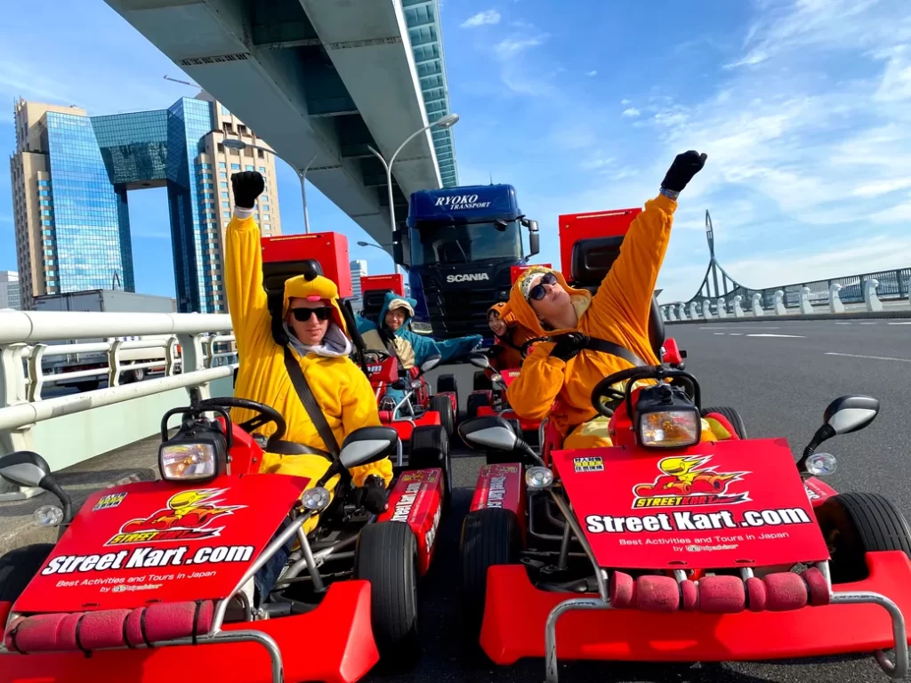 Group of people in bright costumes riding red go-karts on a city bridge, branding visible on the karts.